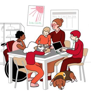 An einem Tisch sitzen vier Kinder mit einer Lehrerin. Ein schwarzes Mädchen sitzt im Rollstuhl. Ein Mädchen und ein Junge machen etwas mit Papier. Ein anderen Junge macht etwas an einem Computer. Zu seinen Füßen liegt ein Assistenzhund.